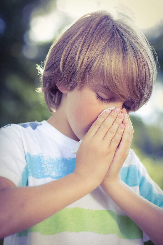 young blonde boy blowing his nose in tissue