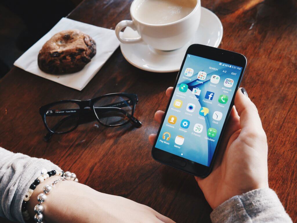 person holding phone with donut and coffee cup