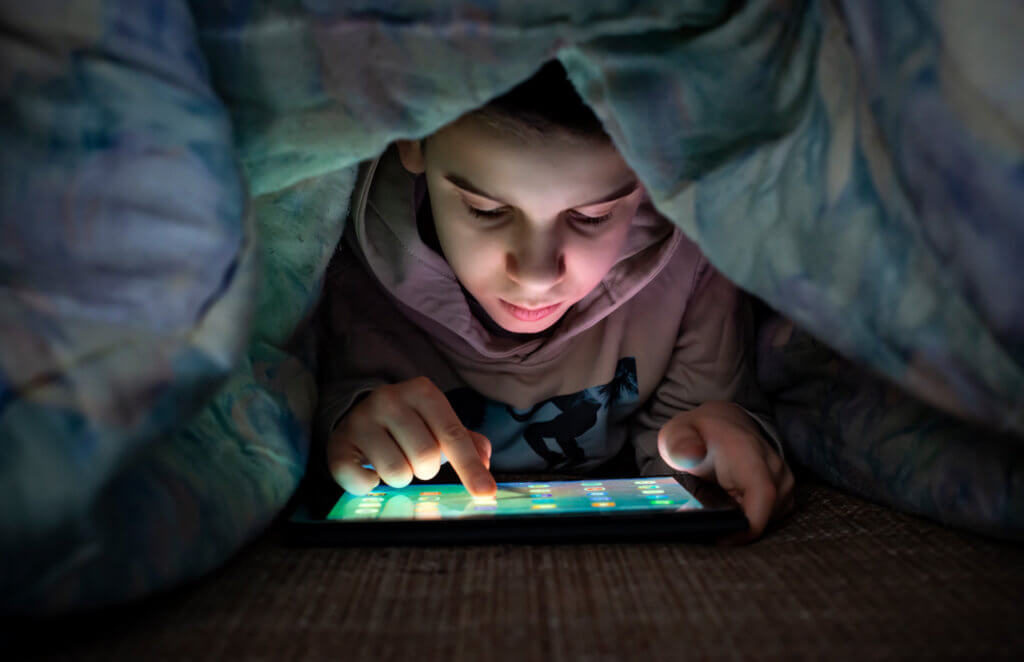 young boy looking at tablet under covers