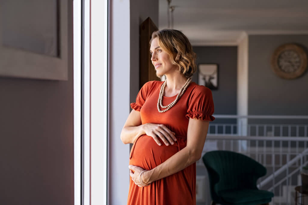 an older pregnant woman standing next to window