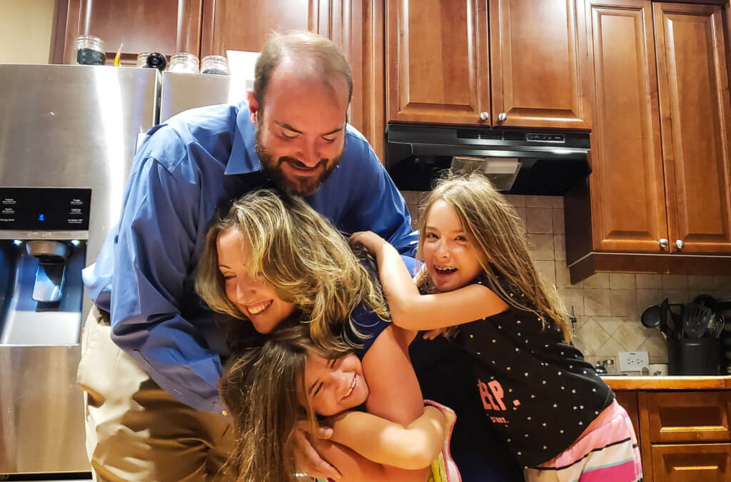 mom, dad and two little girls hugging in the kitchen