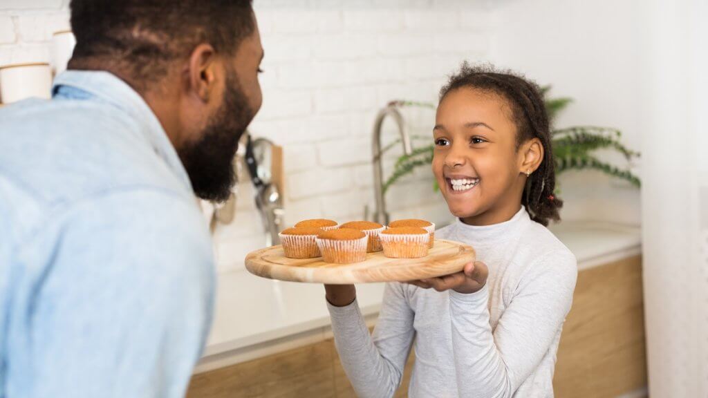 young girl showing her dad a plate of muffins