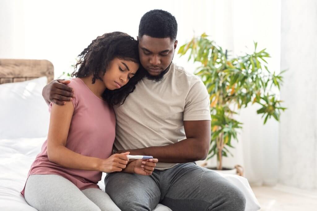 a young Black couple holding a pregnancy test looking sad