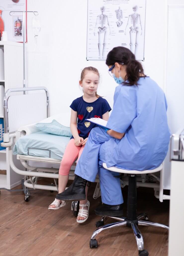 a nurse holding a clipboard talking to a young child in the doctor's office
