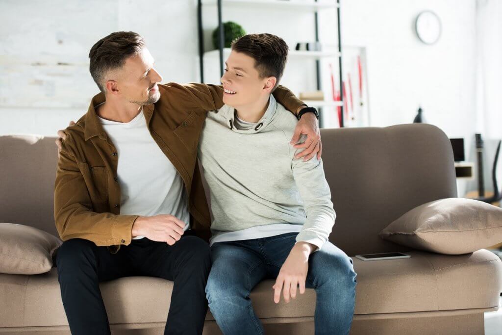 happy father and teen son hugging on sofa at home