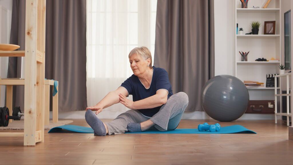 woman stretching legs sitting on yoga mat in living room.