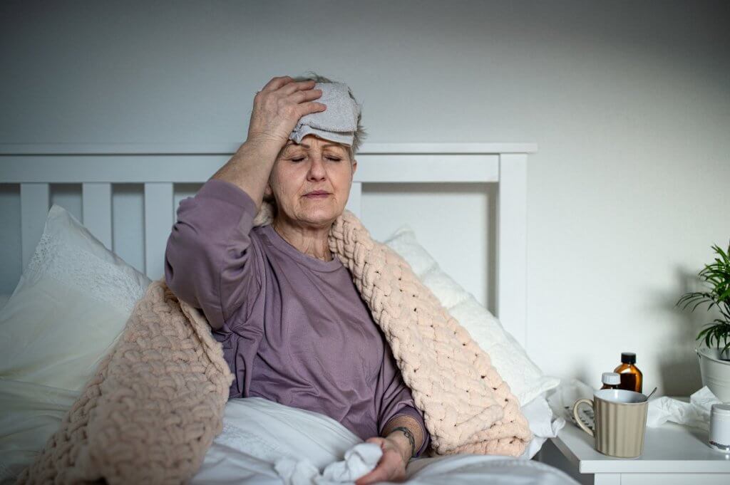 Sick senior woman with headache in bed at home