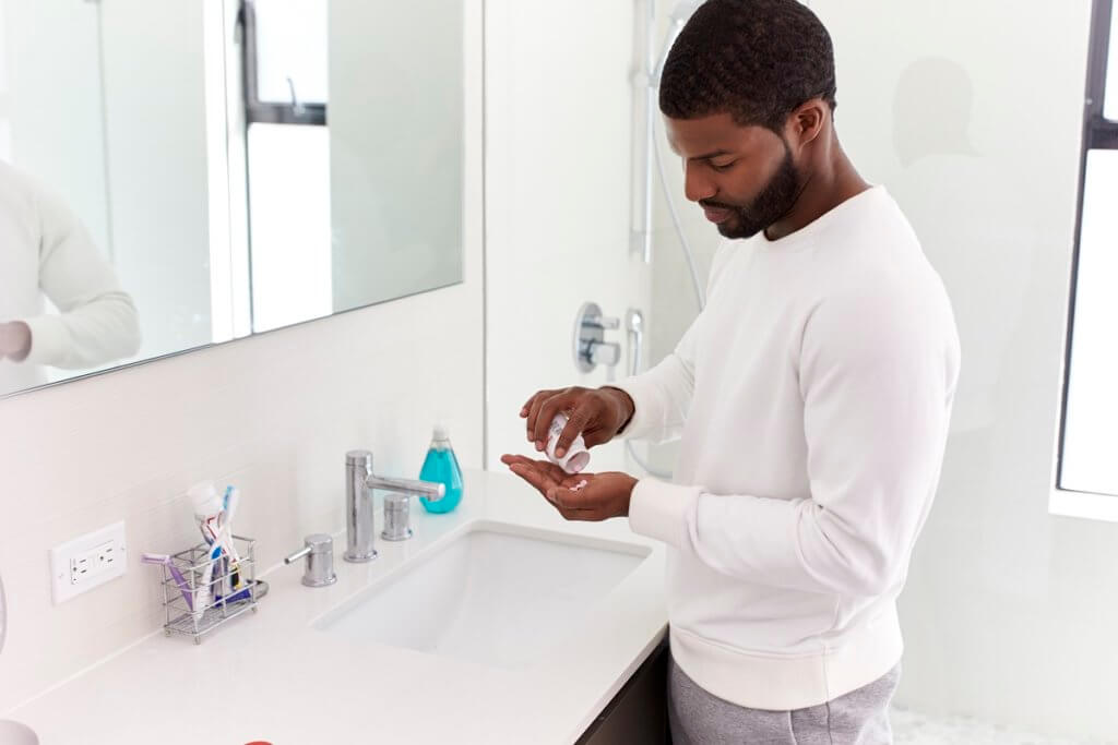 Man In Bathroom Taking Vitamin Supplement Tablets