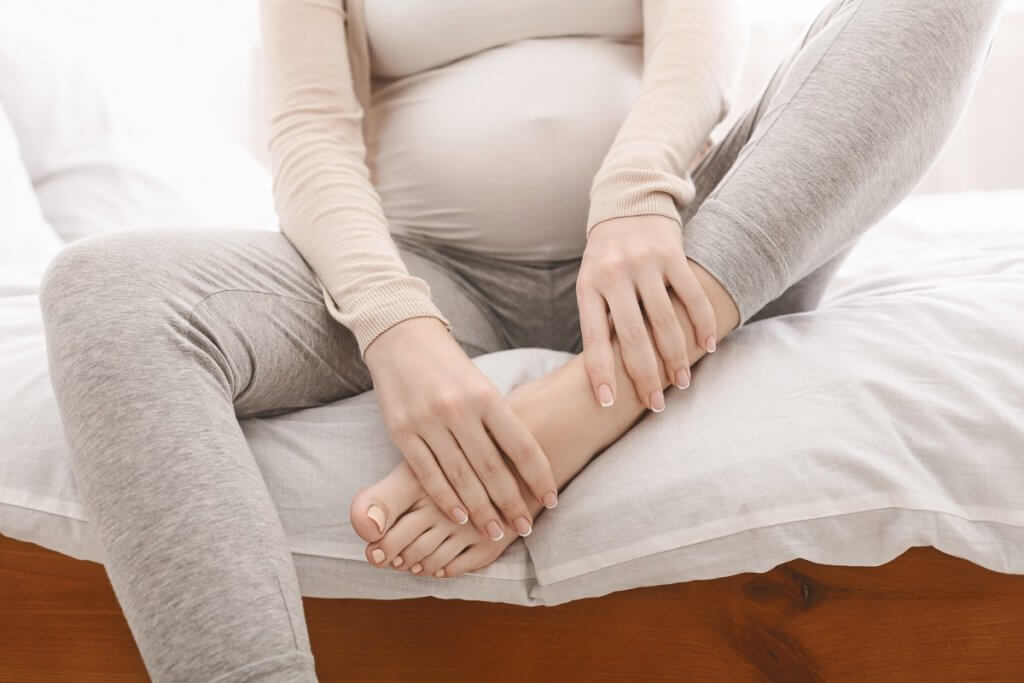 pregnant person sitting on bed massaging feet