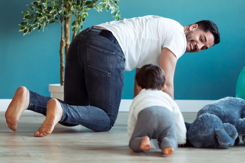 Shot of smiling young father has fun with little baby while are crawling on the floor together at home.