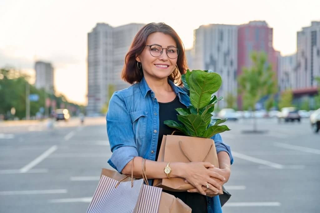 a middle age woman holding shopping bags and a plant