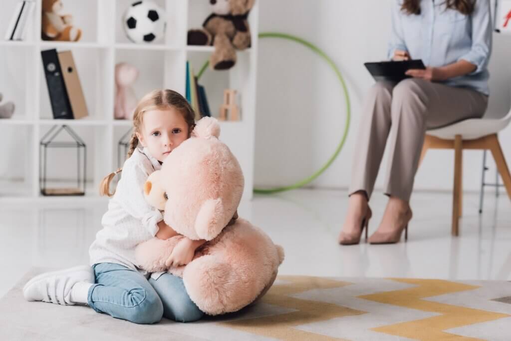 young child sitting on floor with toy bear