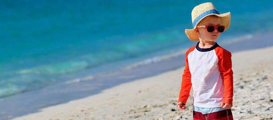 young toddler wearing hat and sunglasses at the beach